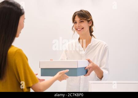 Junge ziemlich positive Modeberater glücklich geben Schuhe in Box an Kunden im Geschäft Stockfoto
