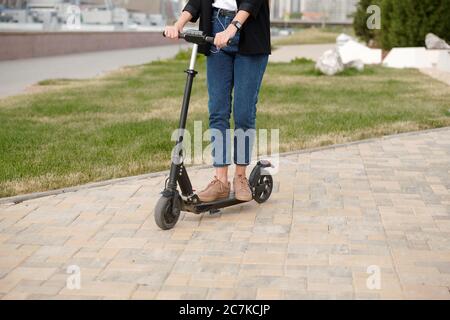 Beine und Hände von jungen zeitgenössischen Frauen in Casualwear stehen auf Elektroroller, während sich nach unten städtischen Straße zur Arbeit Stockfoto