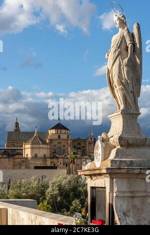 Die Statue des Erzengels San Rafael von Bernabé Gómez del Río scheint von ihrem Sockel auf der Puente Romano aus die Moschee-Kathedrale von Cordoba zu übersehen Stockfoto