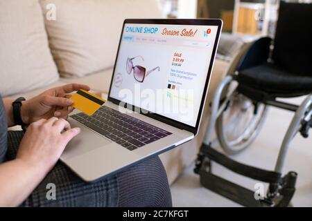 Hände von jungen zeitgenössischen deaktivieren Frau hält Kreditkarte über Laptop-Tastatur, während gehen, um im Online-Shop von zu Hause aus zu machen Stockfoto