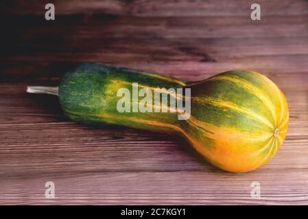 Gelb-grüner länglicher Kürbis, natürlicher Holzhintergrund, Diätnahrung, Halloween Nahaufnahme Stockfoto