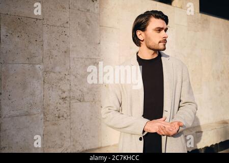 Seitenansicht des jungen, hübschen Mannes im Mantel, der nachdenklich nach draußen schaute Stockfoto