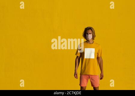 Blonde junge Mann mit Maske auf einem gelben Hintergrund. Sommer Coronavirus Konzept Stockfoto