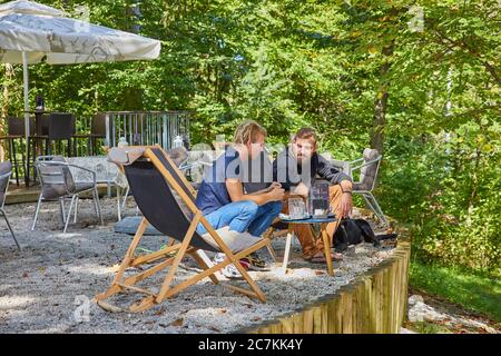 Zwei Männer sprechen, während sie in einem kleinen Café im Freien sitzen Auf dem Land Stockfoto