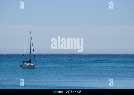 Horizontale Aufnahme mit einem Segelboot links vom Rahmen auf einem ruhigen Meer mit einem hellblauen wolkenlosen Himmel in malaga Stockfoto