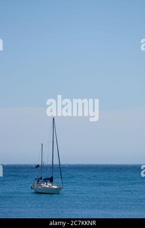 Vertikale Aufnahme mit einem Segelboot links vom Rahmen auf einem ruhigen Meer mit einem hellblauen wolkenlosen Himmel in malaga Stockfoto