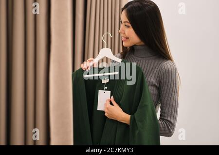 Seitenansicht von ziemlich lächelnd asiatische Mädchen freudig versuchen auf Strickjacke im Mode-Shop Stockfoto