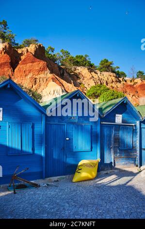 Europa, Portugal, Algarve, Litoral, Barlavento, Bezirk Faro, bei Albufeira, Praia dos Olhos de Agua, blaue Fischerhütten vor rotbraunen Klippen, Hochformat Stockfoto