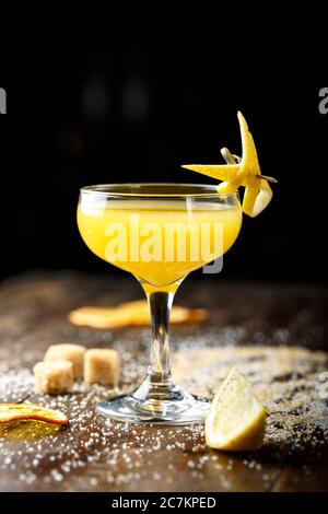 Gelbe tropischen Cocktail in einem eleganten Glas auf einer hölzernen Tresen. Rohrzucker ist neben dem Glas. Platz für Text Stockfoto