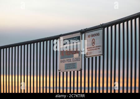 Warnschilder in der Nähe des Strandes auf einem Metallzaun während Sonnenuntergang Stockfoto