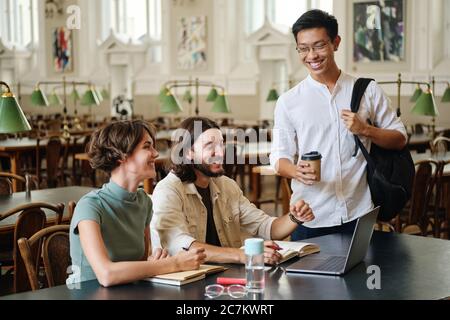 Die Gruppe der jungen fröhlichen Studenten, die sich freudig unterhalten, während sie zusammen in der Bibliothek der Universität studieren Stockfoto