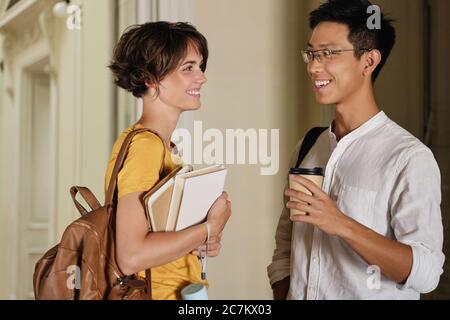 Zwei junge attraktive lächelnde beiläufige internationale Studenten freudig im Korridor der Universität zu sprechen Stockfoto