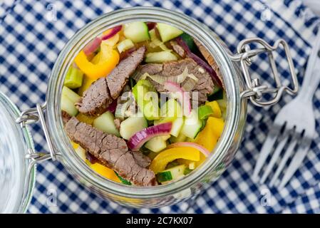 Nahaufnahme, Einmachglas mit Rindfleischsalat auf blauem und weißem kariertem Tuch. Stockfoto