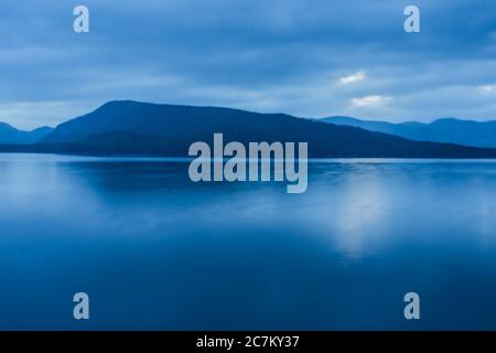 Atemberaubende Aufnahme eines tiefblauen Ozeans und eines Berges An einem trüben Tag Stockfoto