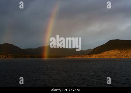 Atemberaubende Aufnahme eines tiefblauen Ozeans und eines Berges An einem bewölkten Tag mit Regenbogen Stockfoto