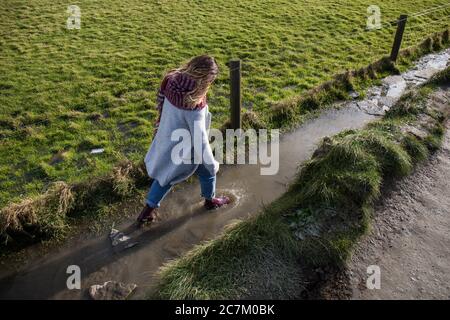 High-Angle-Aufnahme einer Frau, die auf einem schlammigen Weg ist Straße mit Gummistiefeln Stockfoto