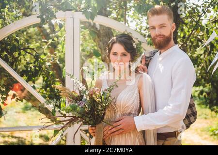 Hochzeit Porträt von stilvollen Bräutigam und nette Braut im Park Grün im Garten. Schöne Brautpaare umarmen zärtlich auf Hintergrund rustikalen Holzhochzeit Stockfoto