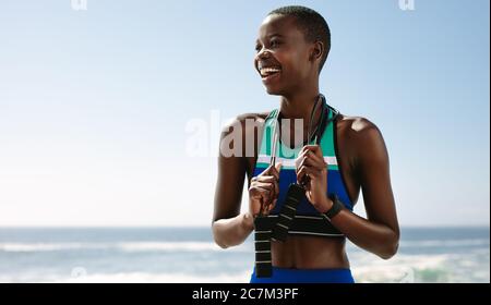 Eine junge Frau mit Sprungseil steht draußen. Fitness-Frau mit Seilspringen, wegschauend und lächelnd. Stockfoto