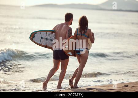 Junges kaukasisches Paar, das am Meer entlang läuft und Surfbretter hält Stockfoto