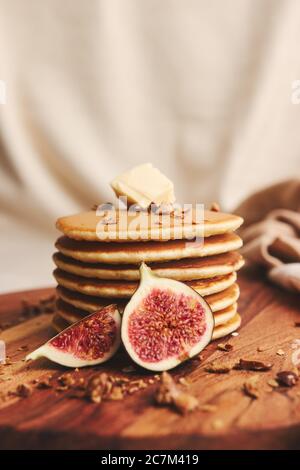 Vertikale Aufnahme von Pfannkuchen mit Sirup, Butter, Feigen und gerösteten Nüssen auf einem Holzteller Stockfoto