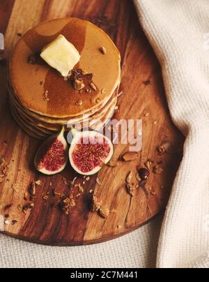 Vertikale Aufnahme von Pfannkuchen mit Sirup, Butter, Feigen und gerösteten Nüssen auf einem Holzteller Stockfoto