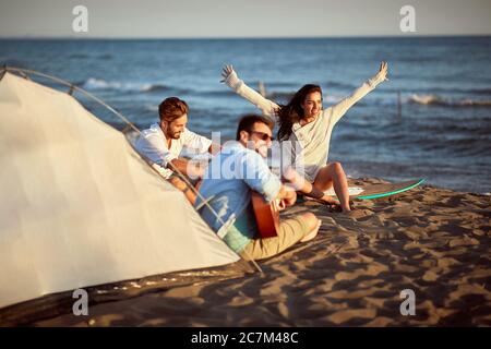 Gruppe von Freunden singen am Strand, genießen den Sonnenuntergang, lächeln, lachen Stockfoto
