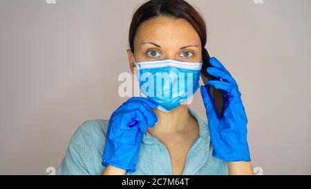 Ärztin Arzt oder Krankenschwester trägt Schutzmaske und Latexhandschuhe, während sie auf dem Handy spricht. Stockfoto