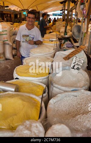 Ein Mann an seinem Stand, der Säcke mit Produkten zum Verkauf arrangiert, hält inne, um sich die Kamera auf dem Markt in Belem in para State, Brasilien, anzusehen. Stockfoto