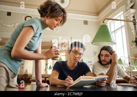 Junge attraktive Tutor helfen multinationalen Studenten mit dem Studium während der Lektion in der Bibliothek der Universität Stockfoto