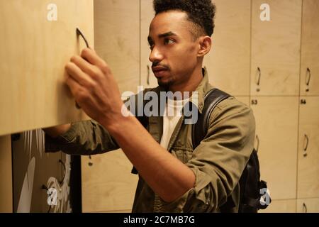 Junge seriöse casual afroamerikanischen Mann verlassen Dinge im Schließfach in Büro Garderobe Stockfoto