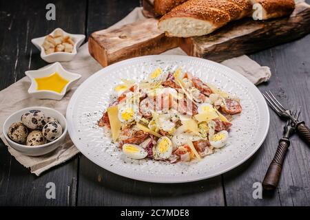 Spanischer Salat mit würzigen Chorizzo-Würsten, Wachteleiern und Käse. Mediterrane Küche Stillleben auf einem dunklen Hintergrund. Nahaufnahme. Stockfoto