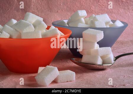Zwei bunte Schüssel und ein Löffel voll mit weißen Zuckerwürfeln. Stockfoto