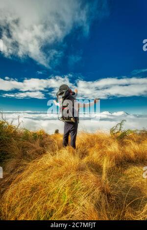 Ein Wanderer, der sein Kind auf dem Rücken trägt, überrascht von Die Landschaft über den Wolken Stockfoto