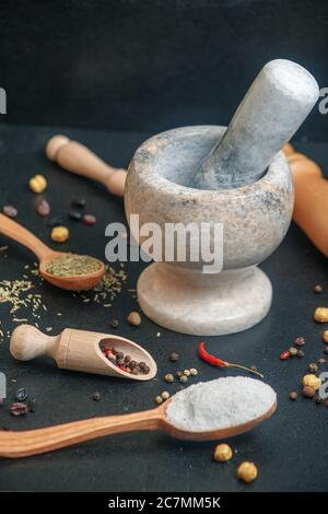 Steinmörtel mit Pfeffer und Holzlöffel mit Gewürzen auf dem Tisch, Seitenansicht Stockfoto