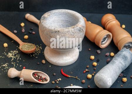 Steinmörtel mit Pfeffer und Holzlöffel mit Gewürzen auf dem Tisch, Seitenansicht Stockfoto