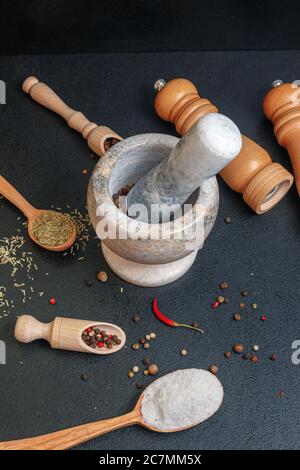 Steinmörtel mit Pfeffer und Holzlöffel mit Gewürzen auf dem Tisch, Seitenansicht Stockfoto