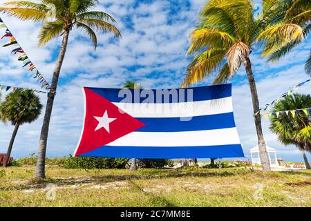 Kubanische Flagge Unter Palmen. Wunderschöne tropische Landschaft im Hintergrund. Kubanische Flagge gegen tropische Palmen und blauen Himmel. Stockfoto