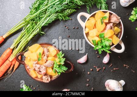 Kartoffelschmorbraten, gebacken mit Fleisch, Schweinefleisch und Petersilie auf einem tiefen Teller neben einem Gewürz numerisch Karotte auf einem schwarzen Tisch. Flach legen, Kopierraum, Draufsicht Stockfoto