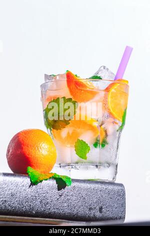 Mandarine Cocktail, Minze, Eis in einem rox Glas am Rand einer Theke weiß Hintergrund. Bot Ansicht, Nahaufnahme, vertikale Ausrichtung Stockfoto