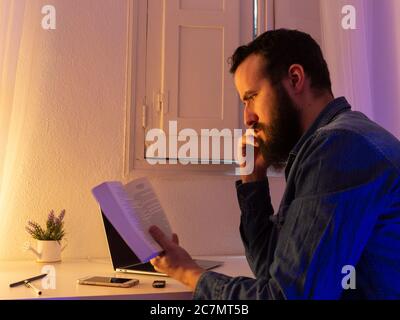 Bärtiger Mann sitzt, hält ein Buch und liest es Stockfoto