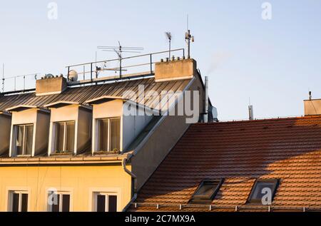 Dach des alten Gebäudes. Dachziegel, Satellit, Antennen und Dachgauben sind auf dem Dach. Klarer blauer Himmel und gelbes Morgen-/Abendlicht Stockfoto