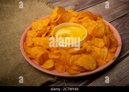 Kartoffelchips auf einer runden Platte und einem Topf mit Käsesauce. Nahaufnahme Stockfoto