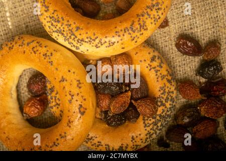 Kleine Bagels und getrocknete Hagebutten, verteilt auf einem homespun Tuch mit einer rauen Textur. Nahaufnahme Stockfoto