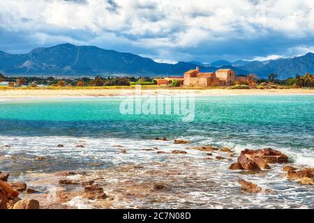 Die Bucht von Nora und der Strand, die mittelalterliche Kirche Sant'Efisio in der Nähe des Ufers und die Berge im Hintergrund. Ort: Nora, Pula, Sardinien, Italien Europa Stockfoto