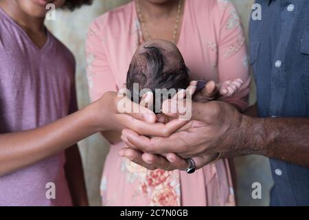 Eine schwarze/afroamerikanische Familie, die ein Baby hält, wobei der Kopf des Babys in den Händen liegt. Stockfoto