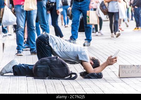 Ein obdachloser junger Mann mit einem Rückzieher mit einem Schild, das besagt: 'Hilf mir bitte', Barcelona, Spanien. Stockfoto