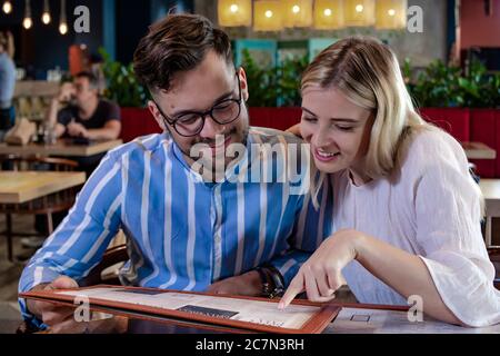 Glückliches junges romantisches Paar, das Essen vom Menü zum Abendessen in einem wunderschönen schicken Restaurant auswählt. Stockfoto