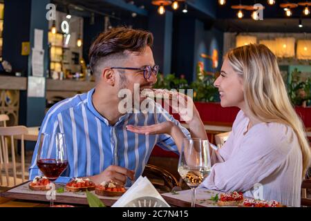 Happy junge romantische Paar in der Liebe Fütterung einander mit Bruschetta beim Abendessen in einem schönen schicken Restaurant. Stockfoto