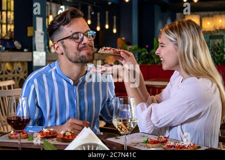 Happy junge romantische Paar in der Liebe Fütterung einander mit Bruschetta beim Abendessen in einem schönen schicken Restaurant. Stockfoto