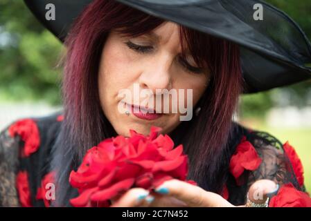 Frau schnuppert den Duft von schönen roten Rosensträuchern in einem botanischen Garten. Stockfoto